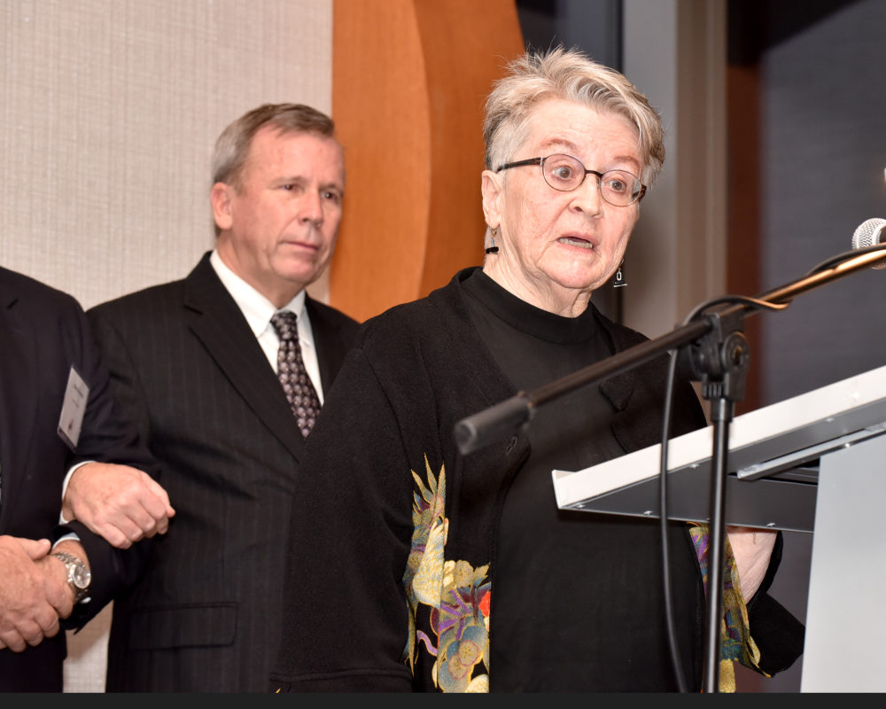 Pamela Heinrich MacPherson, talks about Inductee Frank Heinrich at the Induction into the Hall of Fame ceremony. Behind her are Heinrich family members.